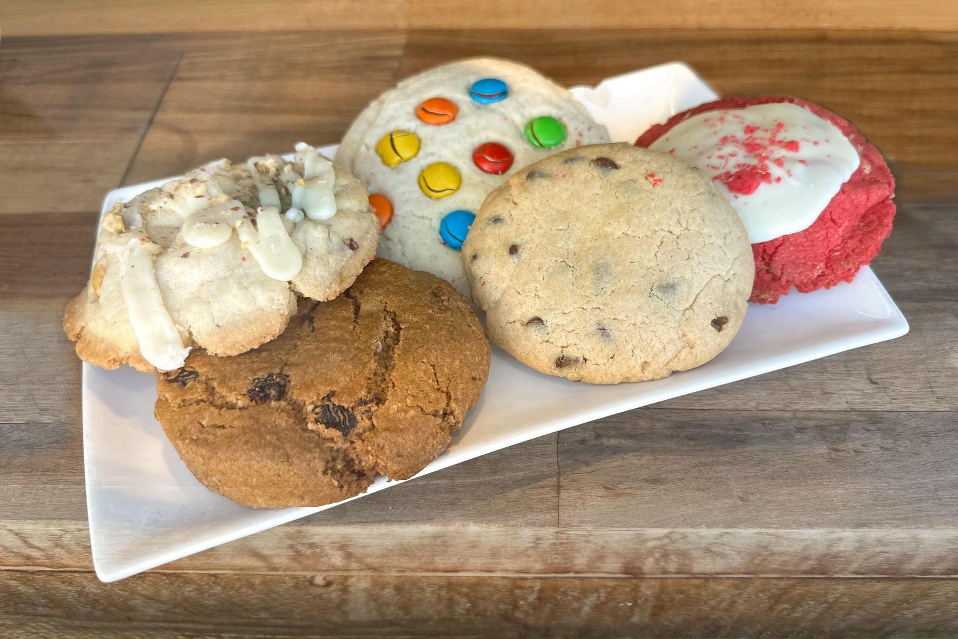 assorted cookies on a white plate placed on a rustic wooden table.